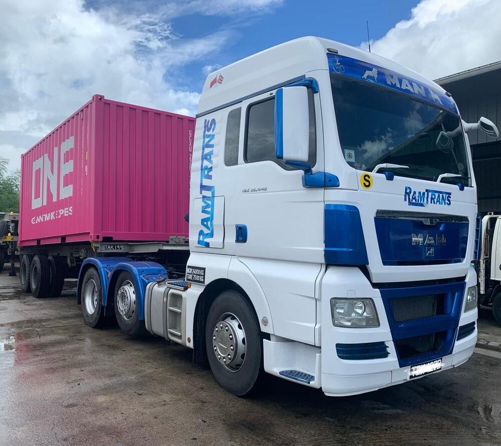A white and blue Ramtrans MAN TGX tractor unit parked beside a 20ft ONE shipping container on a chassis trailer